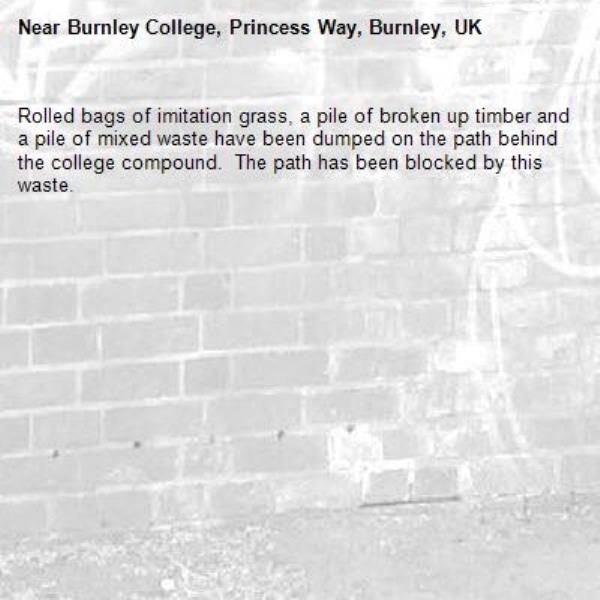 Rolled bags of imitation grass, a pile of broken up timber and a pile of mixed waste have been dumped on the path behind the college compound.  The path has been blocked by this waste.-Burnley College, Princess Way, Burnley, UK