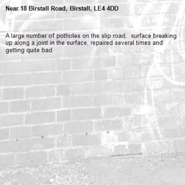 A large number of potholes on the slip road,  surface breaking up along a joint in the surface, repaired several times and getting quite bad-18 Birstall Road, Birstall, LE4 4DD