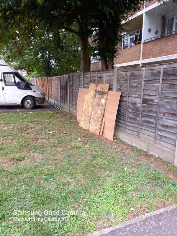 Chipboards left by the fence on the grassed area in the back of Pear Tree Houses near the garages.-Pear Tree House, Brockley Rd, London SE4 2RY near the garages area