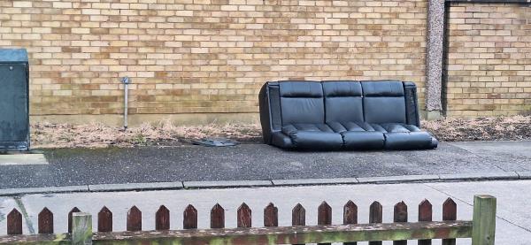 Black sofa on grass varge. Already been dragged down the road into my close by kids from outside the flats on Dupont Gardens. -76 Dupont Gardens, Leicester, LE3 8LB