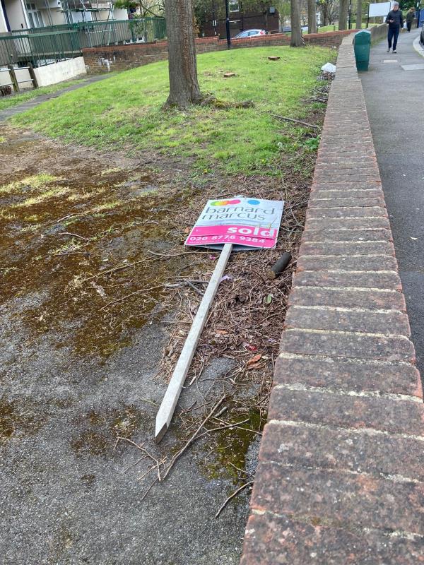 This Bernard Marcus sign remains lying behind the wall by the footpath. It was previously reported but the report was closed without the sign being removed. -1 Lockwood Close, London, SE26 4HY