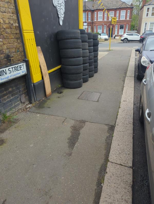 Tire shop piling used tires on pavement. They are here permanently and obstruct pedestrians-1 Benin Street, Hither Green, London, SE13 6UB