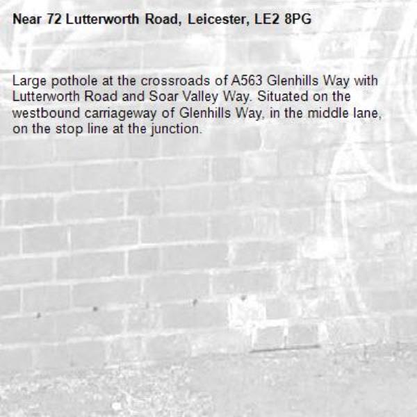 Large pothole at the crossroads of A563 Glenhills Way with Lutterworth Road and Soar Valley Way. Situated on the westbound carriageway of Glenhills Way, in the middle lane, on the stop line at the junction.-72 Lutterworth Road, Leicester, LE2 8PG